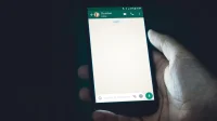Tangan memegang ponsel yang menampilkan jendela obrolan WhatsApp kosong di ruangan gelap