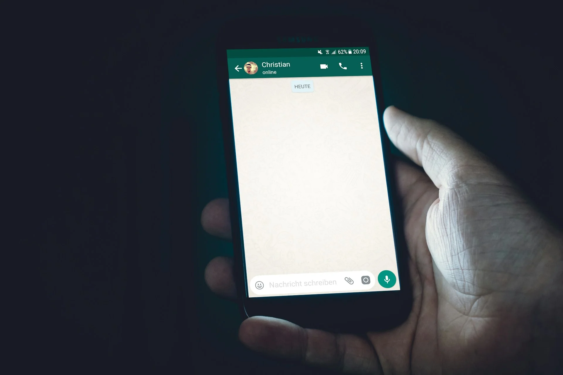 Tangan memegang ponsel yang menampilkan jendela obrolan WhatsApp kosong di ruangan gelap