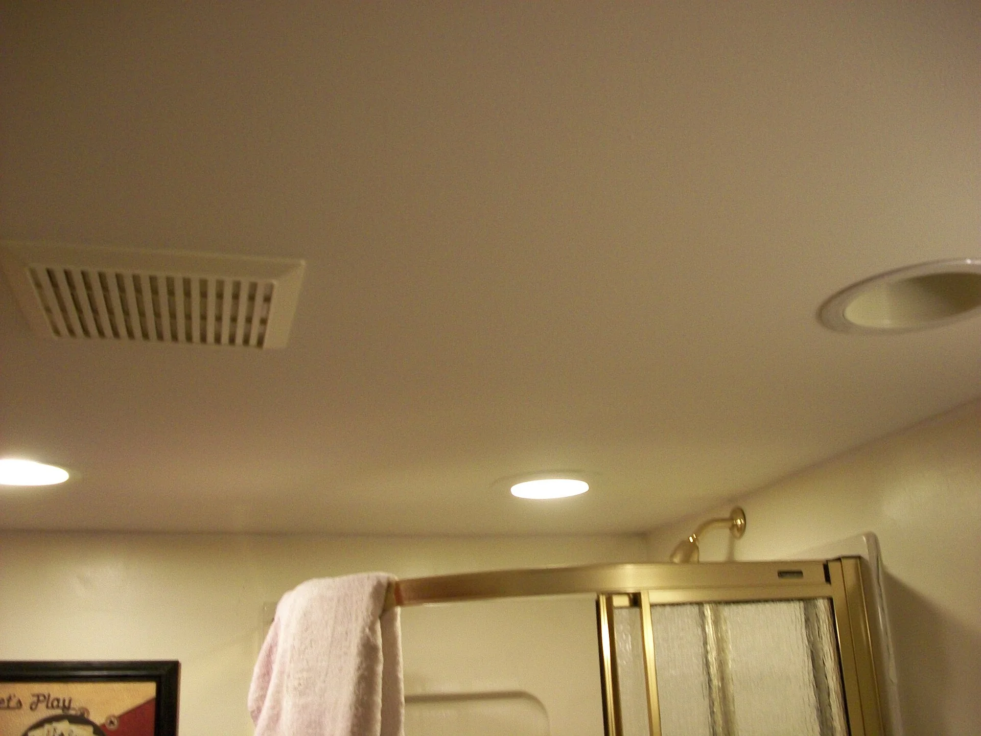 Kisi ventilasi exhaust di plafon kamar mandi dekat bilik shower dan lampu plafon